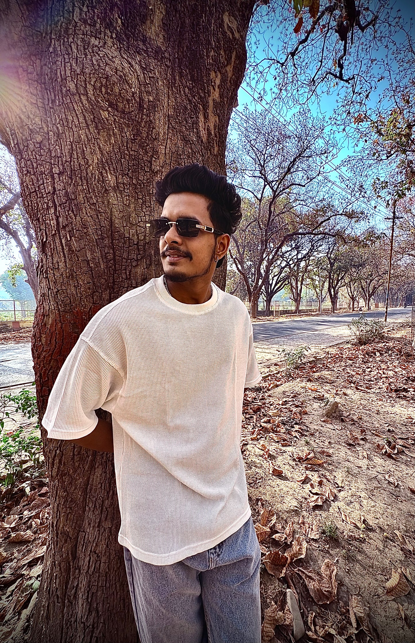 Man standing next to a tree in an outdoor setting with clear sky