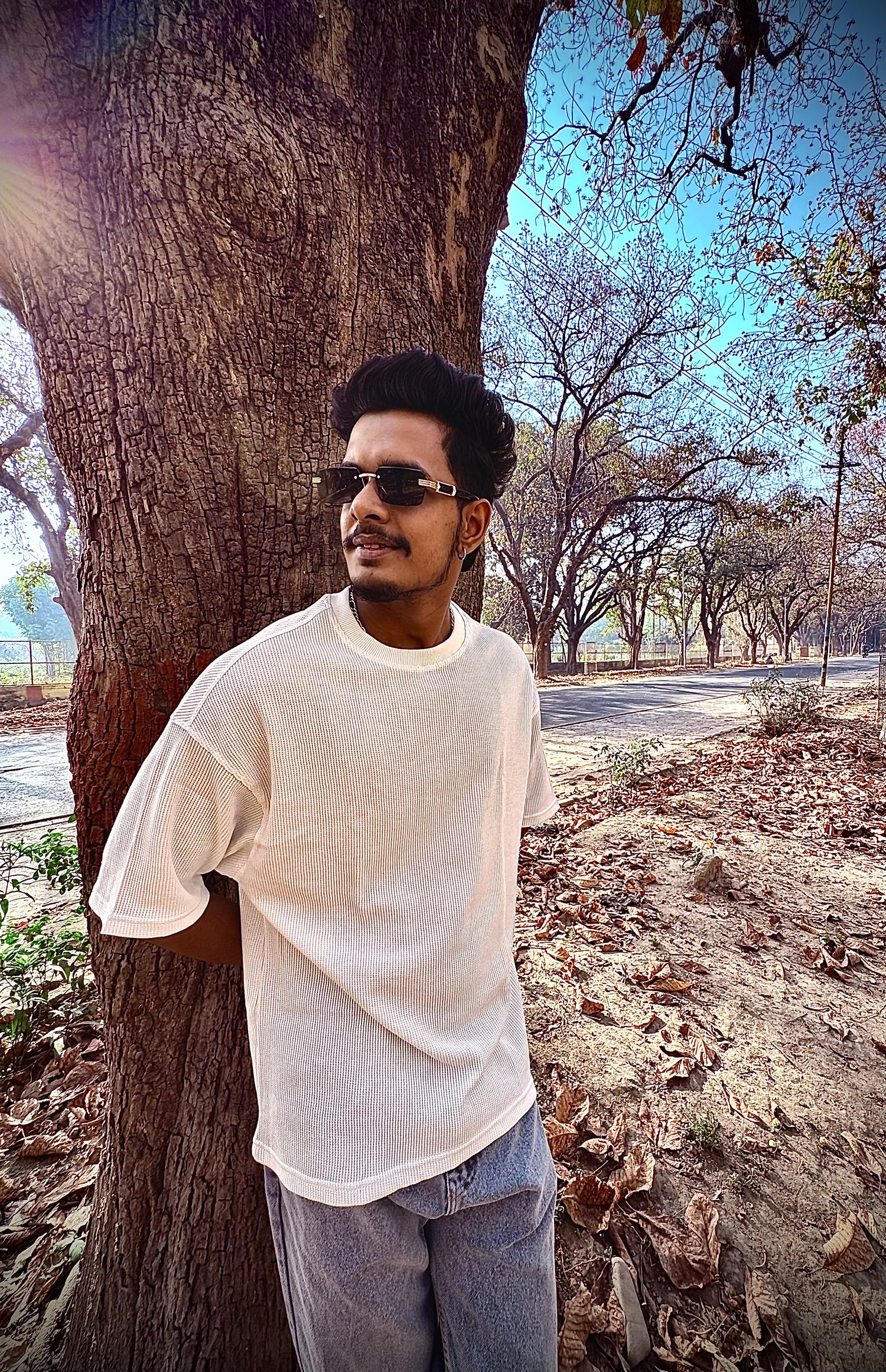 Man standing next to a tree in an outdoor setting with clear sky